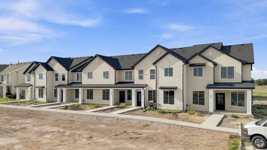 Contemporary townhomes featuring light-colored stucco exteriors, dark shingle roofs, contrasting dark window frames, and covered front porches