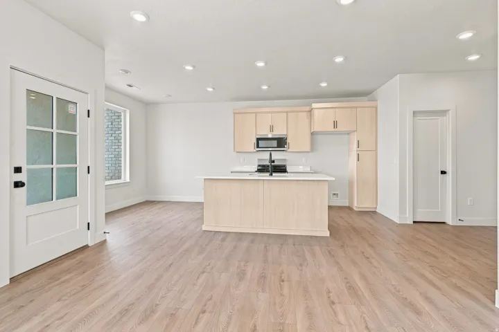 Open-concept kitchen with light wood-finish cabinetry, a central island featuring a sink with a matte black faucet, and stainless steel appliances