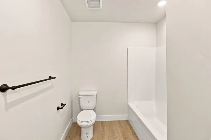 White bathtub with integrated shower, wood-finish flooring, and a white toilet
