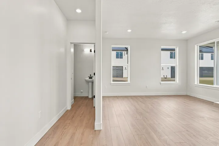 Recessed lighting, light wood-finish flooring, multiple windows, and a pedestal sink with a matte black faucet