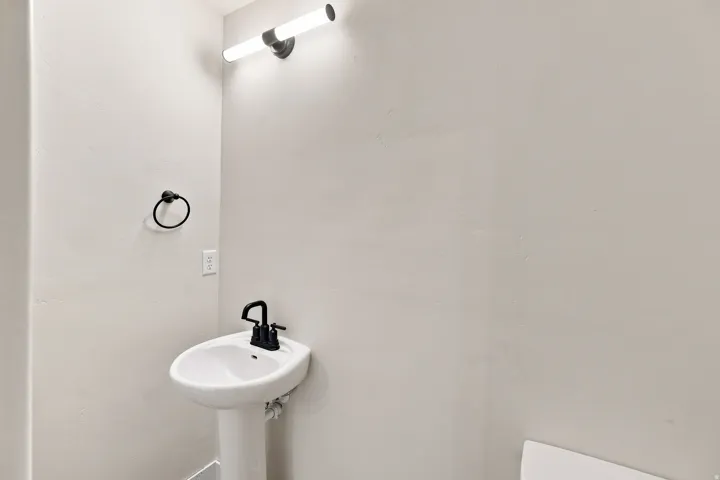 Pedestal sink with a matte black faucet, wall-mounted light fixture, and black towel ring