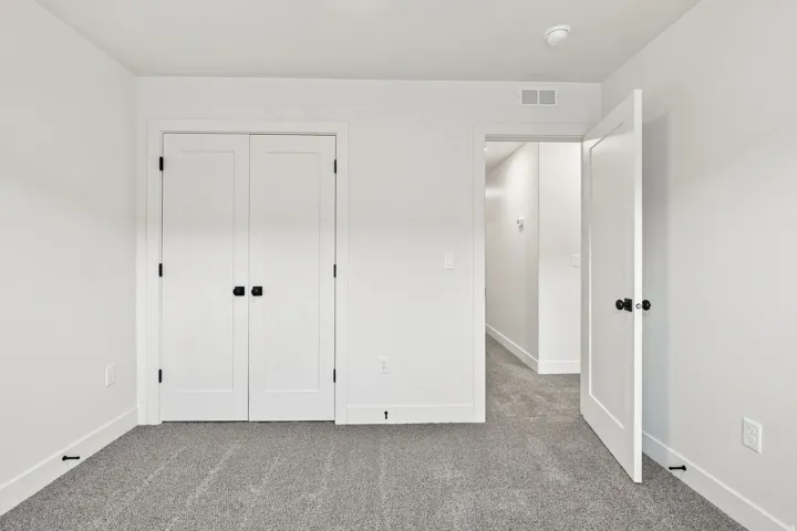 Neutral wall paint, plush carpet flooring, white trim, and white doors with matte black hardware