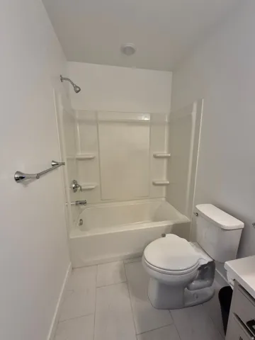 Bathtub with integrated shower, white toilet, chrome fixtures, and tiled flooring