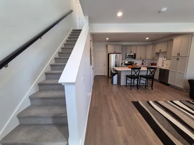 Open-concept kitchen with stainless steel appliances, light-toned cabinetry, a central island, and wood-finish flooring