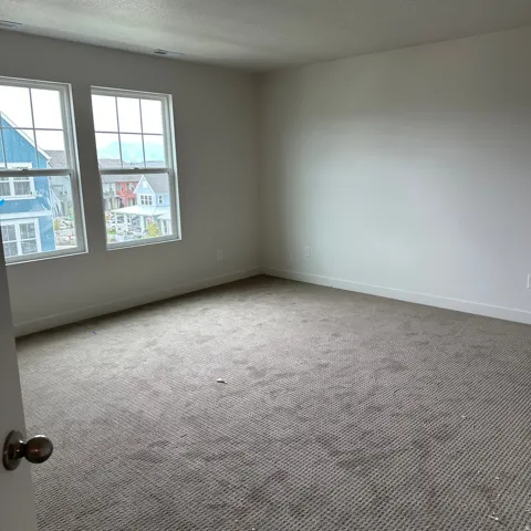 Neutral tone wall finishes, gray textured carpet, and two large windows with grid patterns