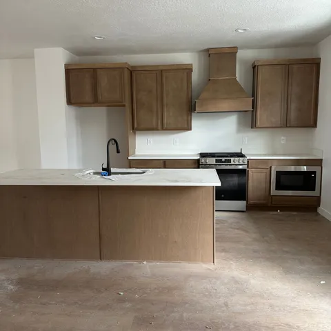 Kitchen featuring a large island with sink, black faucet, light countertops, wood-finish cabinetry, and stainless steel appliances