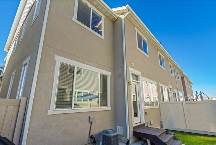 Stucco exterior with multiple windows, leading to a fenced backyard with a wood-finish deck and green space