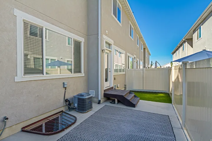 Private outdoor patio with concrete paving, wood-finish steps, and a fenced yard with artificial turf