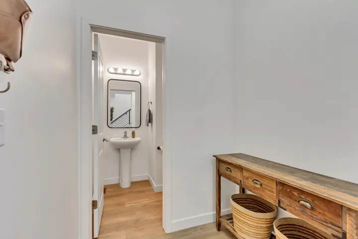Powder room featuring wood-finish flooring, a rectangular framed mirror, a pedestal sink, and a four-bulb vanity light fixture