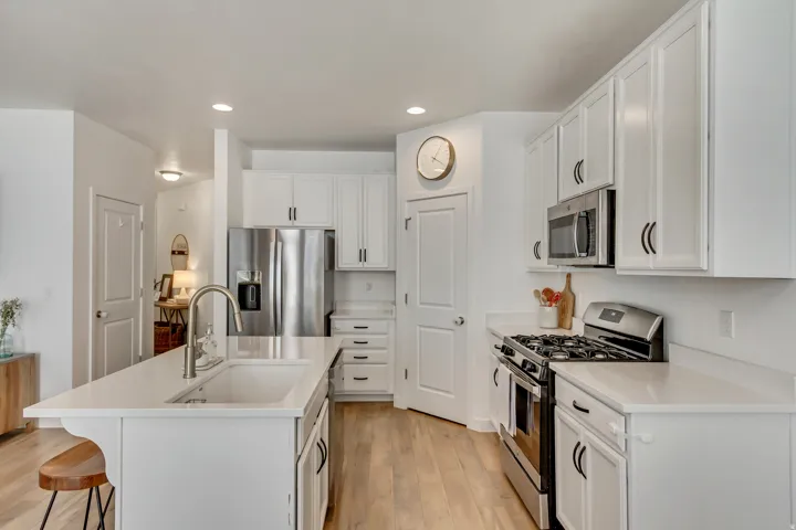 Kitchen featuring white cabinetry, stainless steel appliances, a center island with an undermount sink, recessed lighting, and light wood-finish flooring