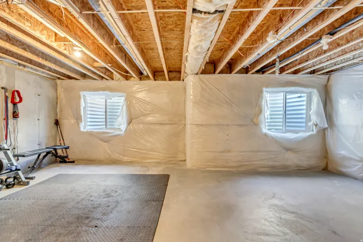 Unfinished basement with exposed ceiling joists, concrete floor, and two windows