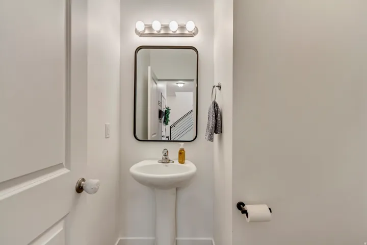 Pedestal sink with chrome faucet, framed rectangular mirror, and a four-bulb vanity light fixture