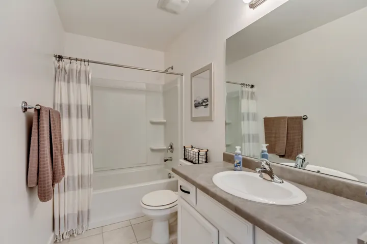 White vanity with a laminate countertop and integrated sink, chrome faucet, wall-mounted mirror, and tile flooring