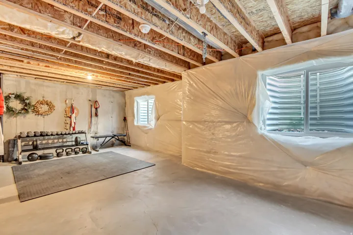 Unfinished basement with exposed ceiling joists, concrete flooring, and egress window