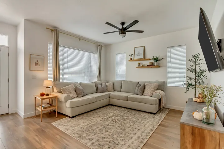 Wood-finish flooring throughout, multiple windows with horizontal blinds, ceiling fan, and built-in floating shelves