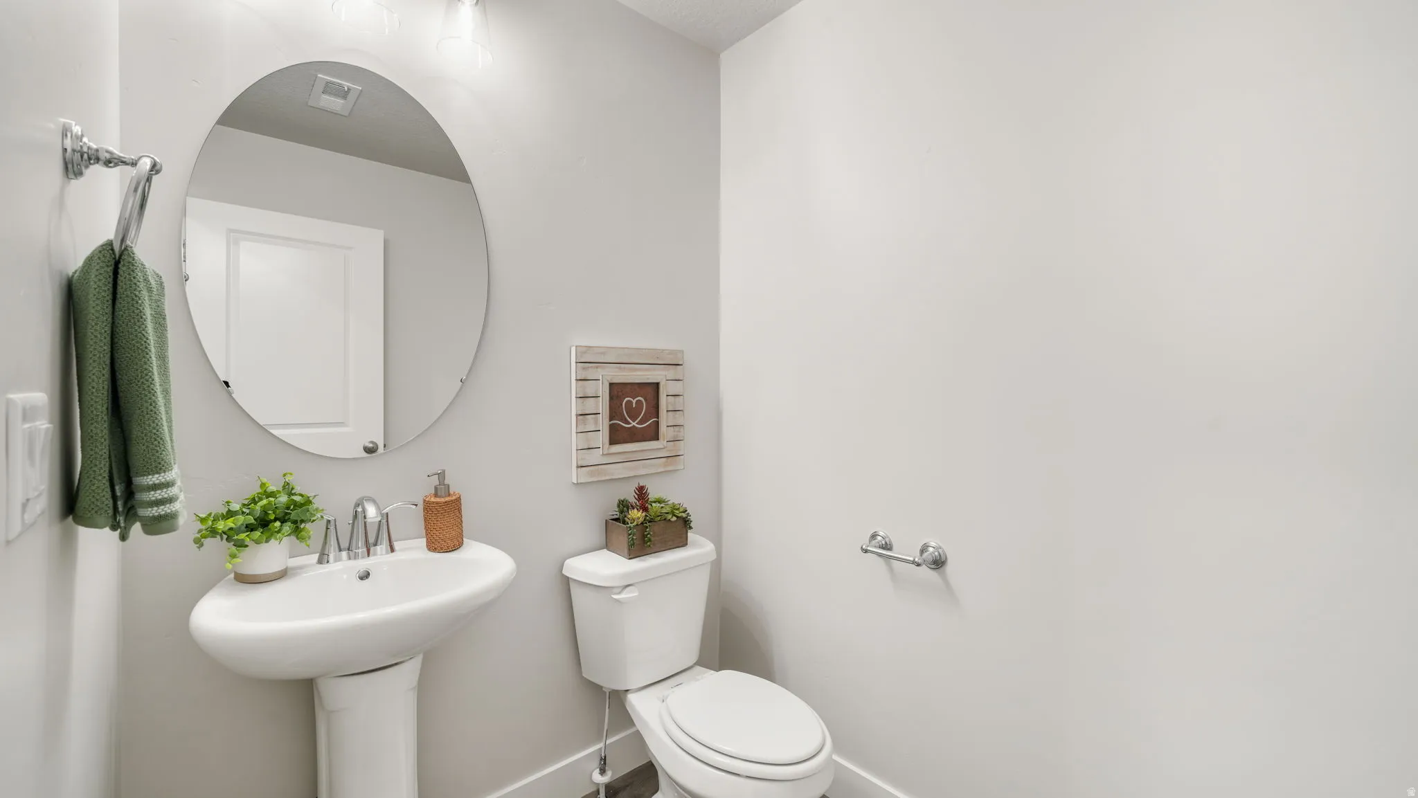 Pedestal sink with a polished chrome faucet, oval mirror, and white toilet