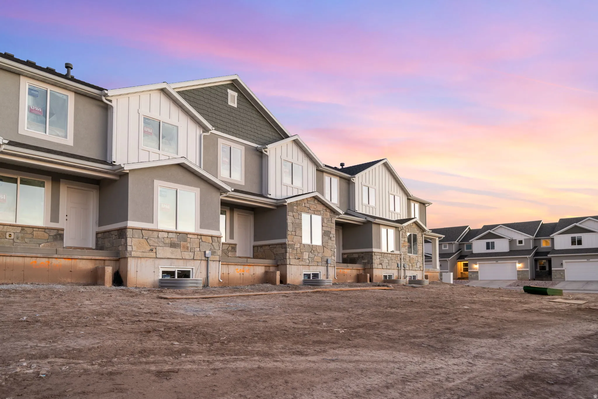 Newly constructed residential units featuring stone and stucco exteriors, multiple windows, and attached garages