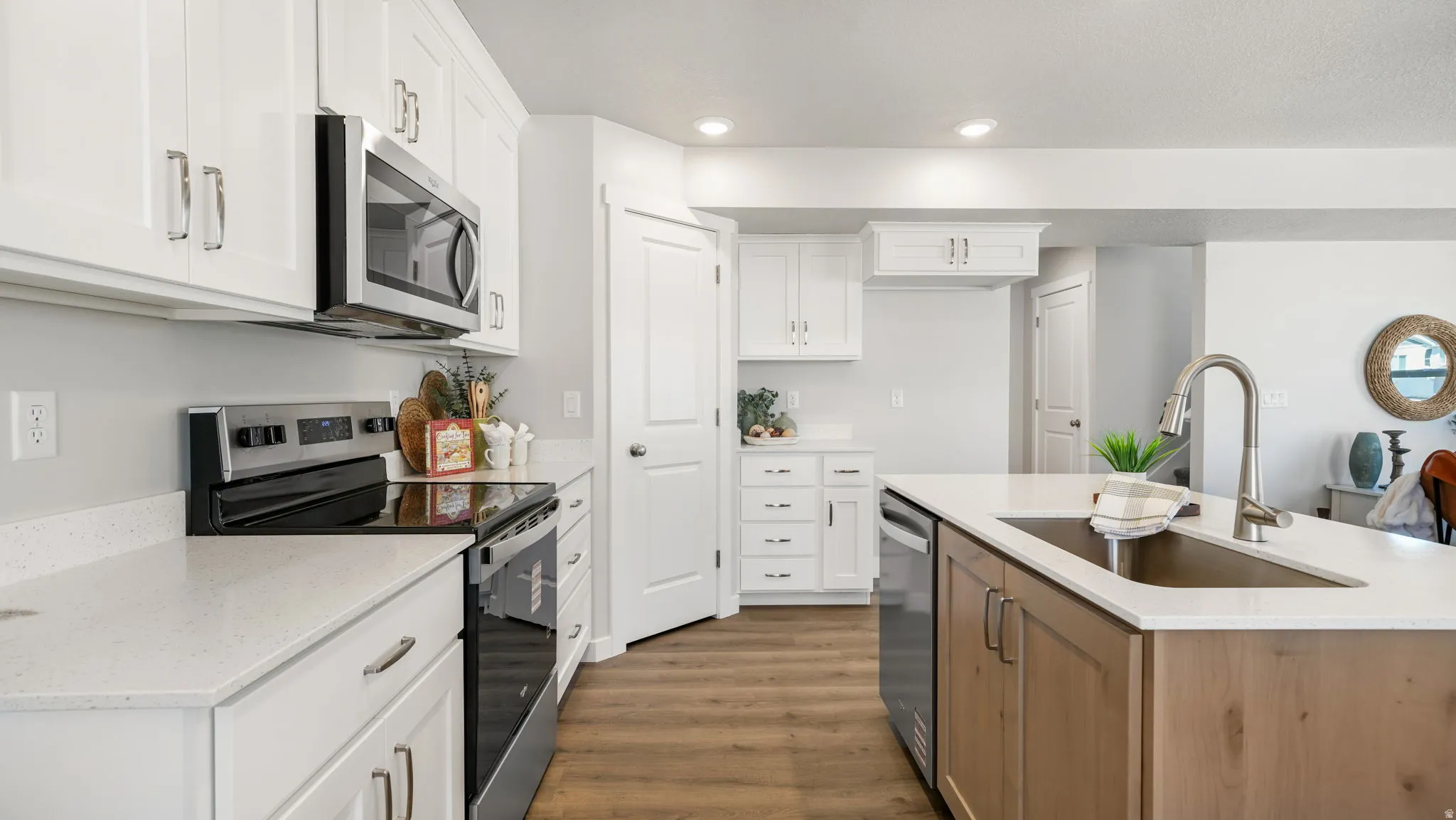 Kitchen featuring white shaker cabinetry, stainless steel appliances, light-toned countertops, wood-finish flooring, and a center island with an undermount sink