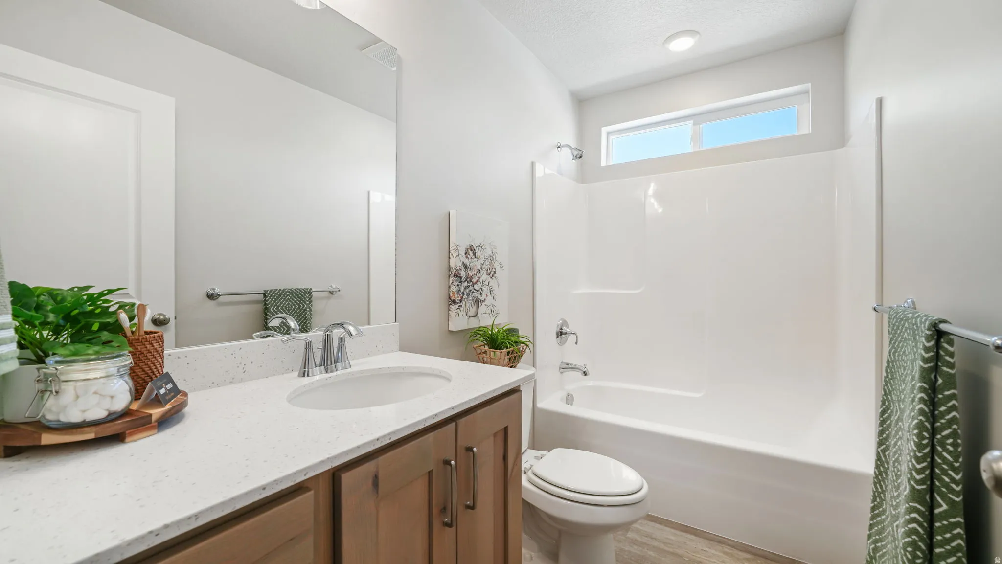 Single vanity with a light-toned countertop, wood-finish cabinetry, and a full-width mirror