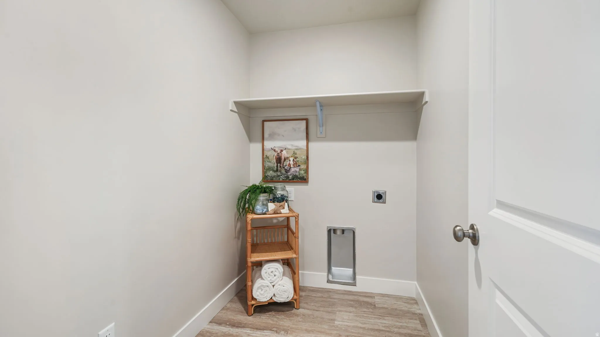 Laundry area with wood-finish flooring, light-toned walls, and a wall-mounted shelf