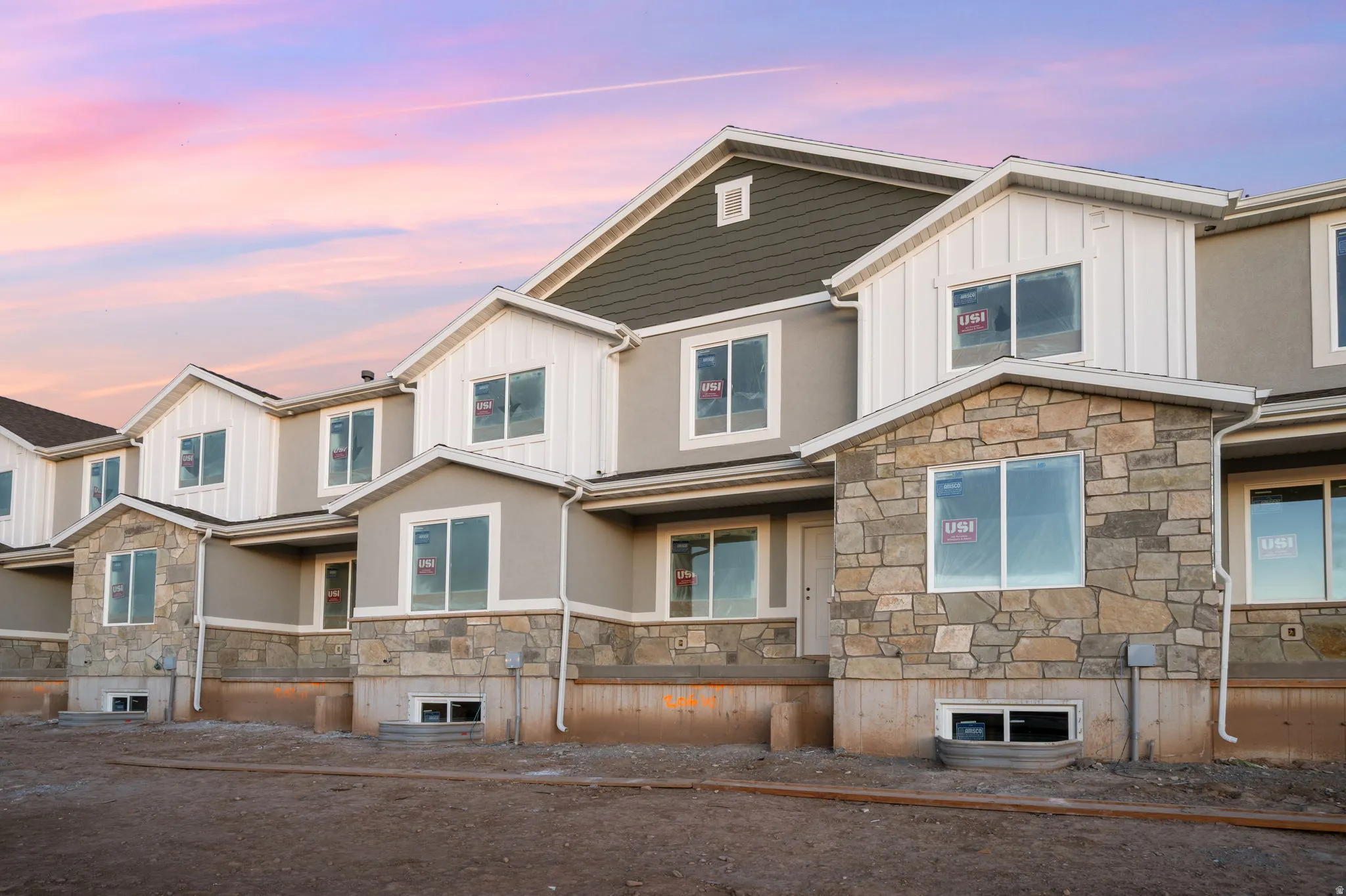 Multi-level facade featuring stone accents, vertical board and batten siding, stucco, and dark shingle roofing