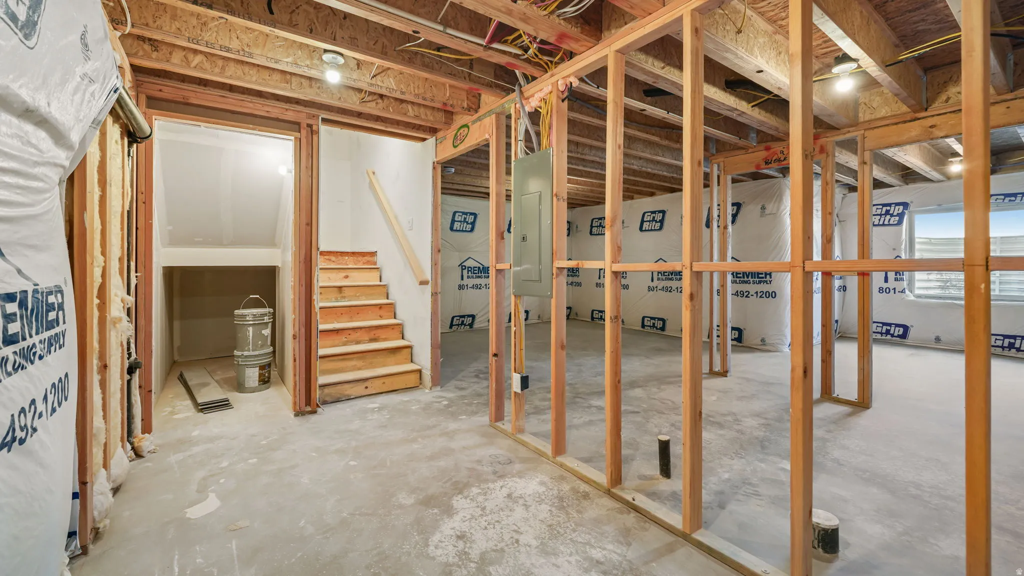 Unfinished basement with exposed wood framing, concrete flooring, recessed lighting, and a wood staircase