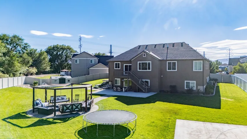 Expansive backyard featuring a large paved patio, a pergola with a circular paver base, a shed, a full privacy fence, and a spacious lawn area