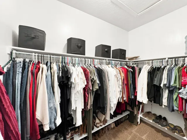 Corner closet featuring multiple hanging rods, integrated shelving, and carpet flooring
