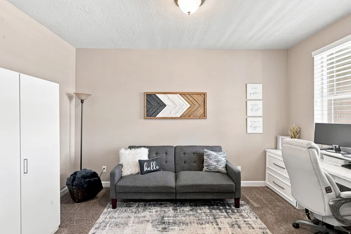 Neutral wall paint, textured ceiling, carpet flooring, window with blinds, and a built-in white storage cabinet