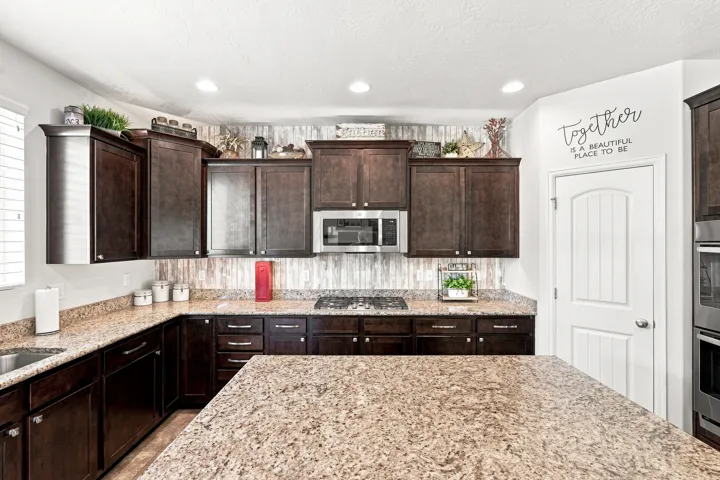 Kitchen featuring dark wood cabinetry, light-toned speckled countertops, and a full stainless steel appliance package