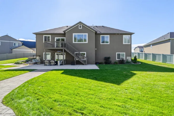 Expansive green lawn, paver pathway, concrete patio, elevated deck with staircase, and lower-level patio access