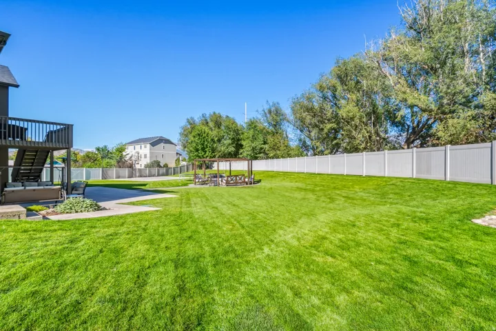Expansive backyard featuring a large concrete patio, a multi-level deck, a wooden pergola, and a privacy fence