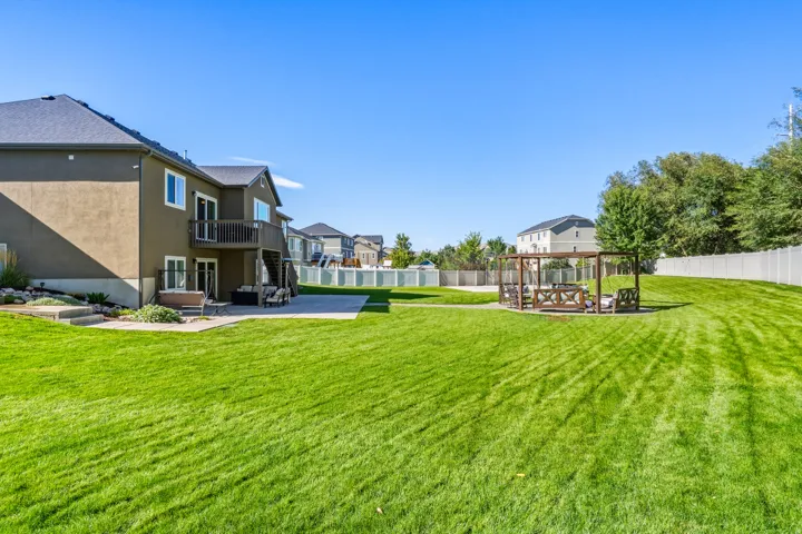 Expansive lawn area, stucco exterior, upper-level balcony, lower-level patio, and a built-in pergola