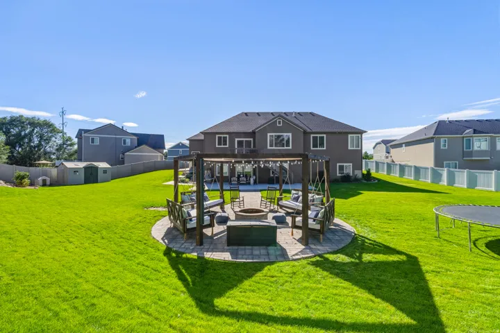 Expansive backyard with a large lawn, a stone paver patio, a pergola, and a fire pit