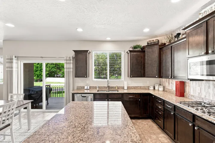 Kitchen featuring dark wood cabinetry, granite countertops, stainless steel appliances, a tile backsplash, and recessed lighting