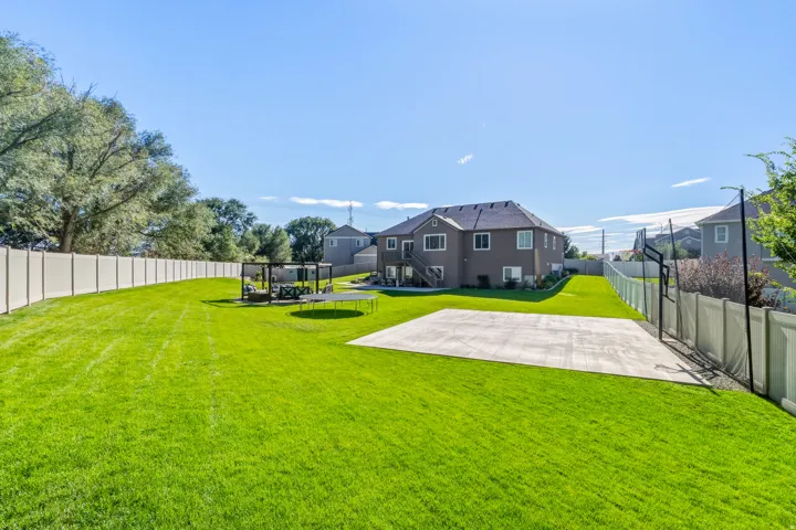Expansive backyard featuring a large lawn, privacy fencing, a concrete sport court, and a pergola