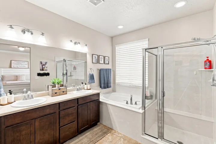 Dual vanity with dark wood-finish cabinetry, built-in soaking tub, glass-enclosed shower, and recessed lighting