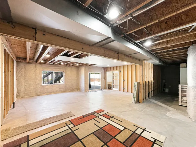 Unfinished lower level with exposed ceiling joists, recessed lighting, framed walls, a window, and an exterior door