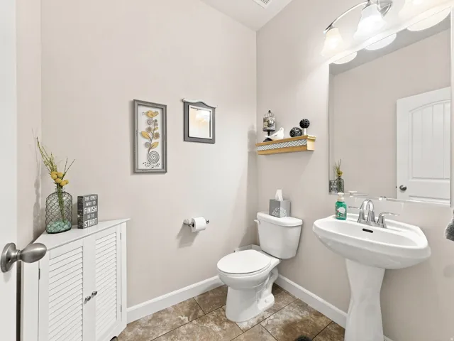 Pedestal sink with chrome faucet, wall-mounted mirror, overhead vanity lighting, and tile flooring