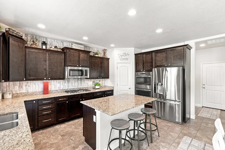 Spacious kitchen featuring dark wood cabinetry, stainless steel appliances, granite countertops, and a central island with bar seating