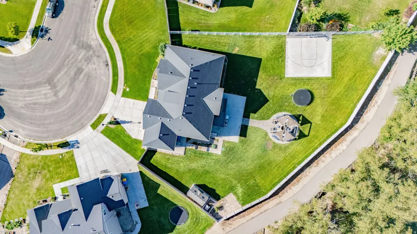 Expansive property featuring a paved sports court, manicured lawn, and multi-level roofline