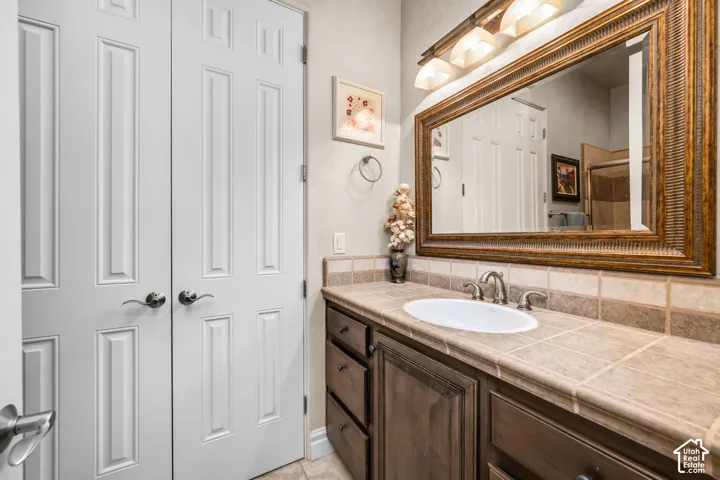 Wood-finish vanity with an integrated sink, tile countertop, and a decorative framed mirror