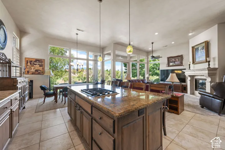 Kitchen island with a built-in cooktop, granite-finish countertop, pendant lighting, and wood-finish cabinetry
