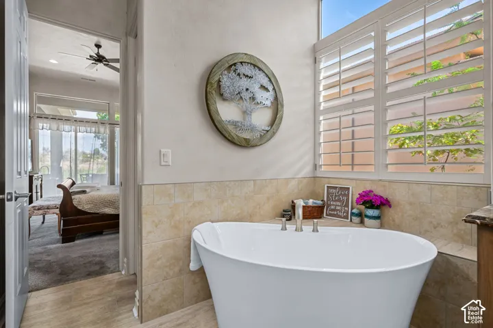 Freestanding soaking tub with brushed nickel fixtures, tiled wainscoting, and plantation shutters