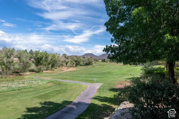 Expansive green space featuring a golf course, paved pathway, surrounding trees, and distant hills