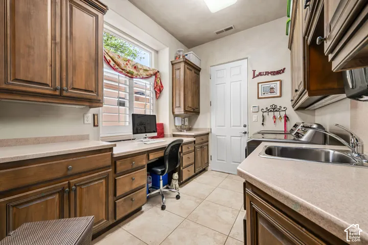 Built-in wood cabinetry with a dedicated desk area, large window with interior shutters, tile flooring, and a utility sink with a stainless steel faucet