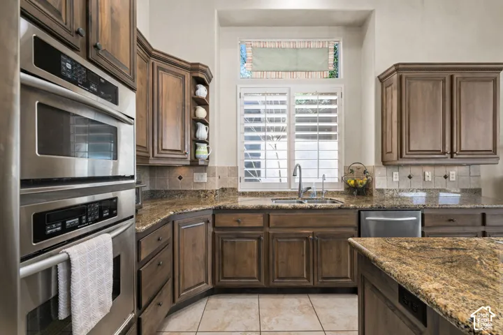 Built-in stainless steel double oven, wood cabinetry, granite countertops, tile backsplash, and stainless steel dishwasher