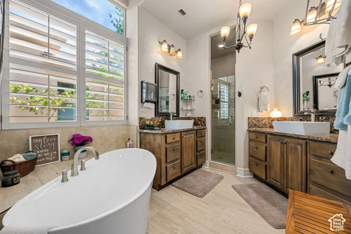 Freestanding soaking tub with brushed nickel fixtures, dual wood-finish vanity cabinets with vessel sinks, framed mirrors, and a glass-enclosed shower