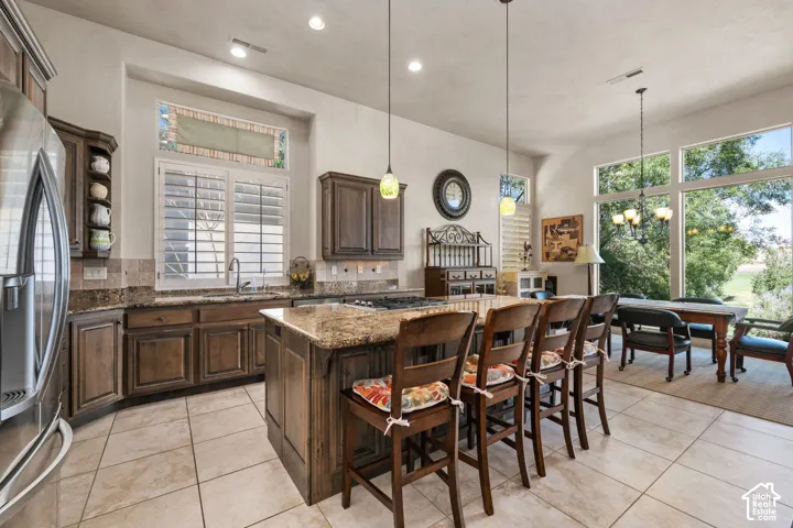 Spacious kitchen featuring an expansive center island with seating, a gas range, dark wood-finish cabinetry, and stone countertops