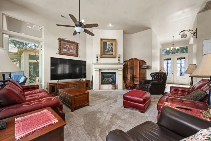 Living area with vaulted ceilings, a stone-faced fireplace, ceiling fan, and double exterior doors